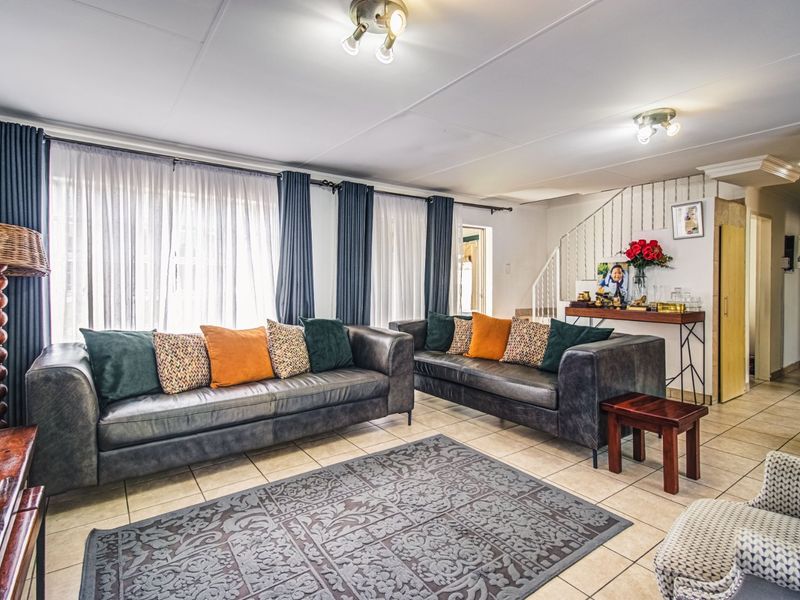 A spacious living room featuring tiled flooring, a staircase, and large windows with curtains, offering a comfortable and functional living space.