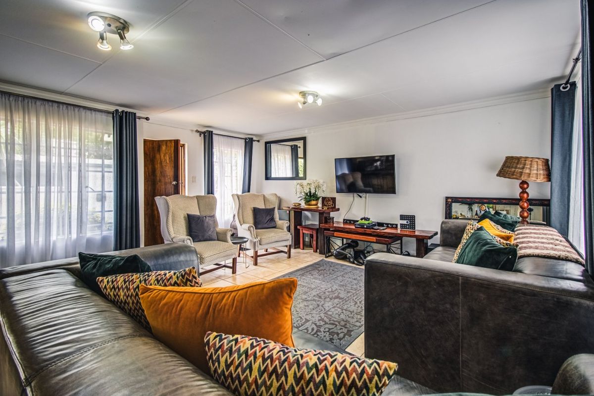 A comfortable living room featuring tiled flooring, ceiling spotlights, and large windows with sliding glass doors providing natural light.