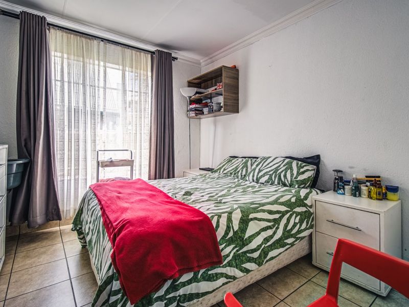 A functional bedroom featuring tiled flooring, built-in shelving, and a sliding glass door providing natural light.
