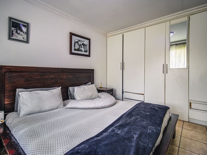 A functional bedroom featuring built-in cupboards with a mirrored panel and tiled flooring, providing practical storage and a neutral foundation.