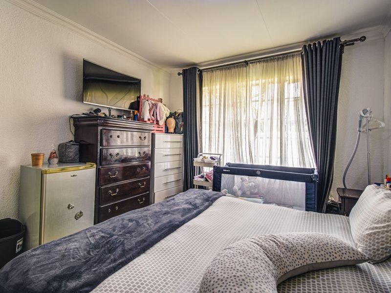A functional bedroom featuring neutral walls, coving, and a large window with installed curtain rails, providing natural light to the space.