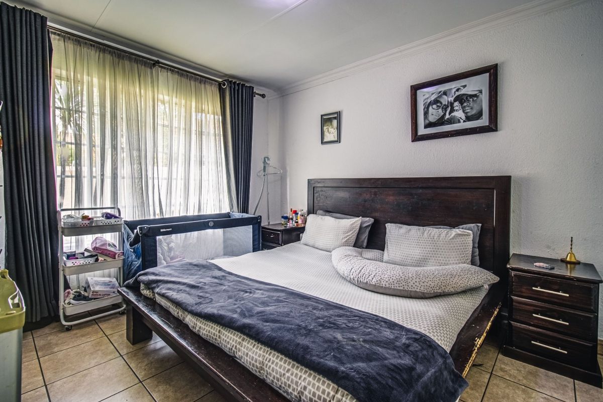 A well-proportioned bedroom featuring tiled flooring, neutral walls, and large windows with curtain rails, offering a comfortable and functional living space.