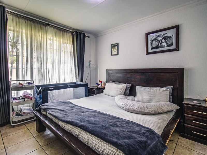 A well-proportioned bedroom featuring tiled flooring, neutral walls, and large windows with curtain rails, offering a comfortable and functional living space.