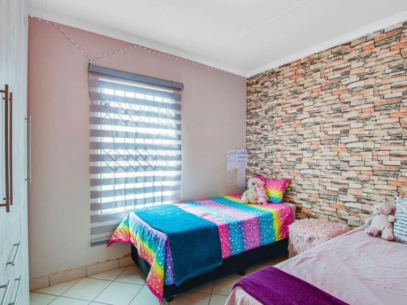 A bedroom featuring tiled flooring, a built-in wardrobe, and a brick-effect feature wall with a window fitted with a roller blind and security gate.