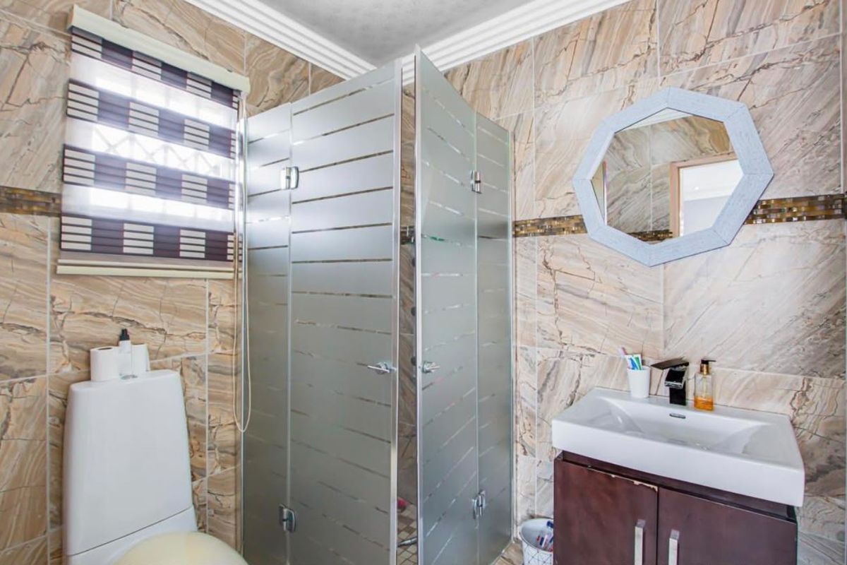A functional bathroom featuring a shower enclosure, vanity basin, and toilet, finished with full-height marble-look wall tiles.