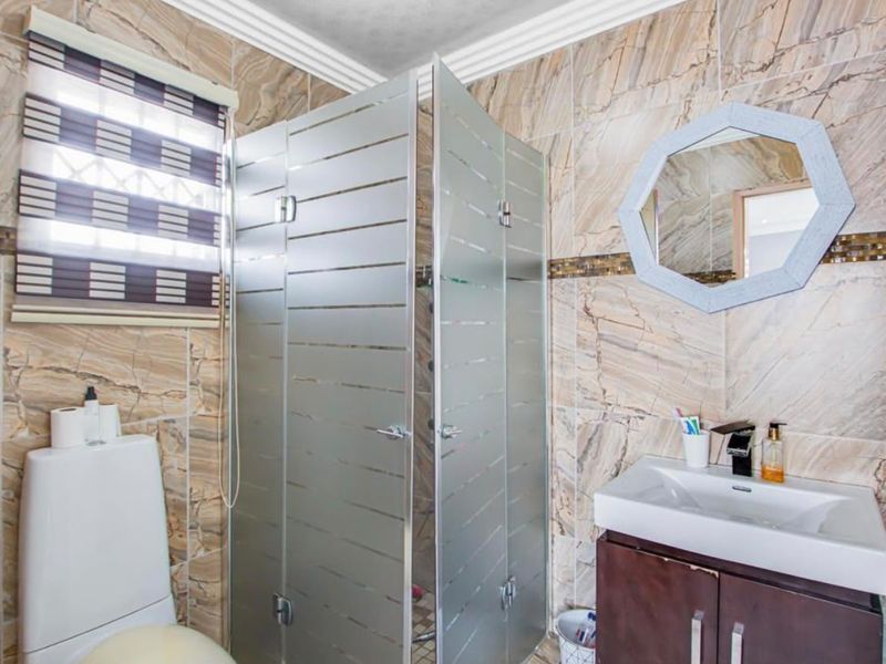 A functional bathroom featuring a shower enclosure, vanity basin, and toilet, finished with full-height marble-look wall tiles.
