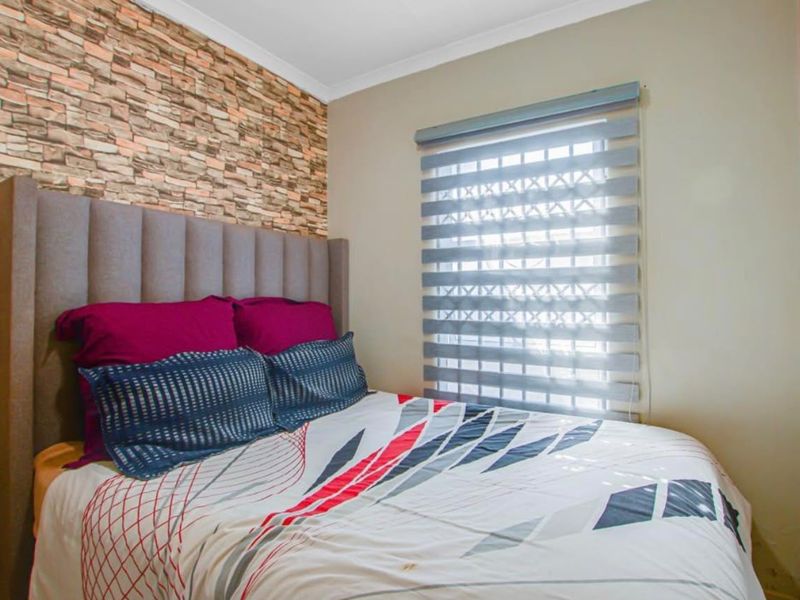 A cozy bedroom featuring a textured stone-look accent wall and a modern dual-layer roller blind.