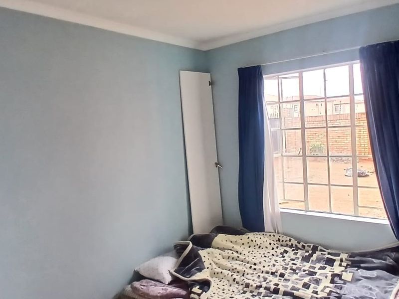 A bedroom featuring light blue walls, a window with security burglar bars, and a built-in cupboard.