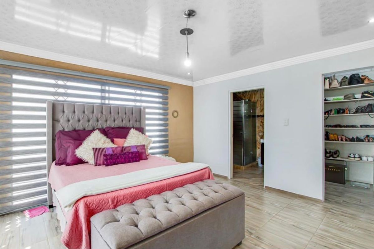 Spacious bedroom featuring tiled flooring, built-in shelving, and an en-suite bathroom access, finished with modern roller blinds and clean neutral wall tones.