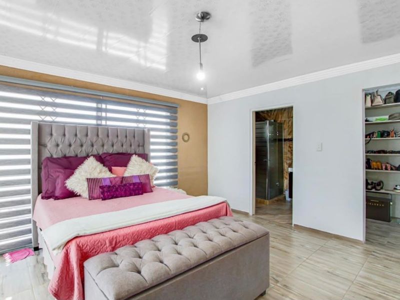 Spacious bedroom featuring tiled flooring, built-in shelving, and an en-suite bathroom access, finished with modern roller blinds and clean neutral wall tones.