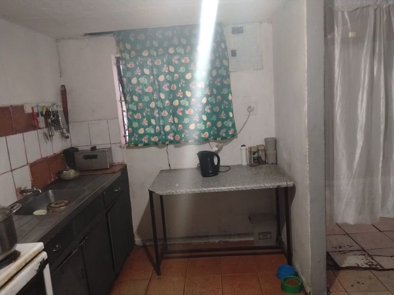A dated kitchen area featuring a built-in sink, tiled splashback, and basic cabinetry, requiring significant renovation to modernize the space.