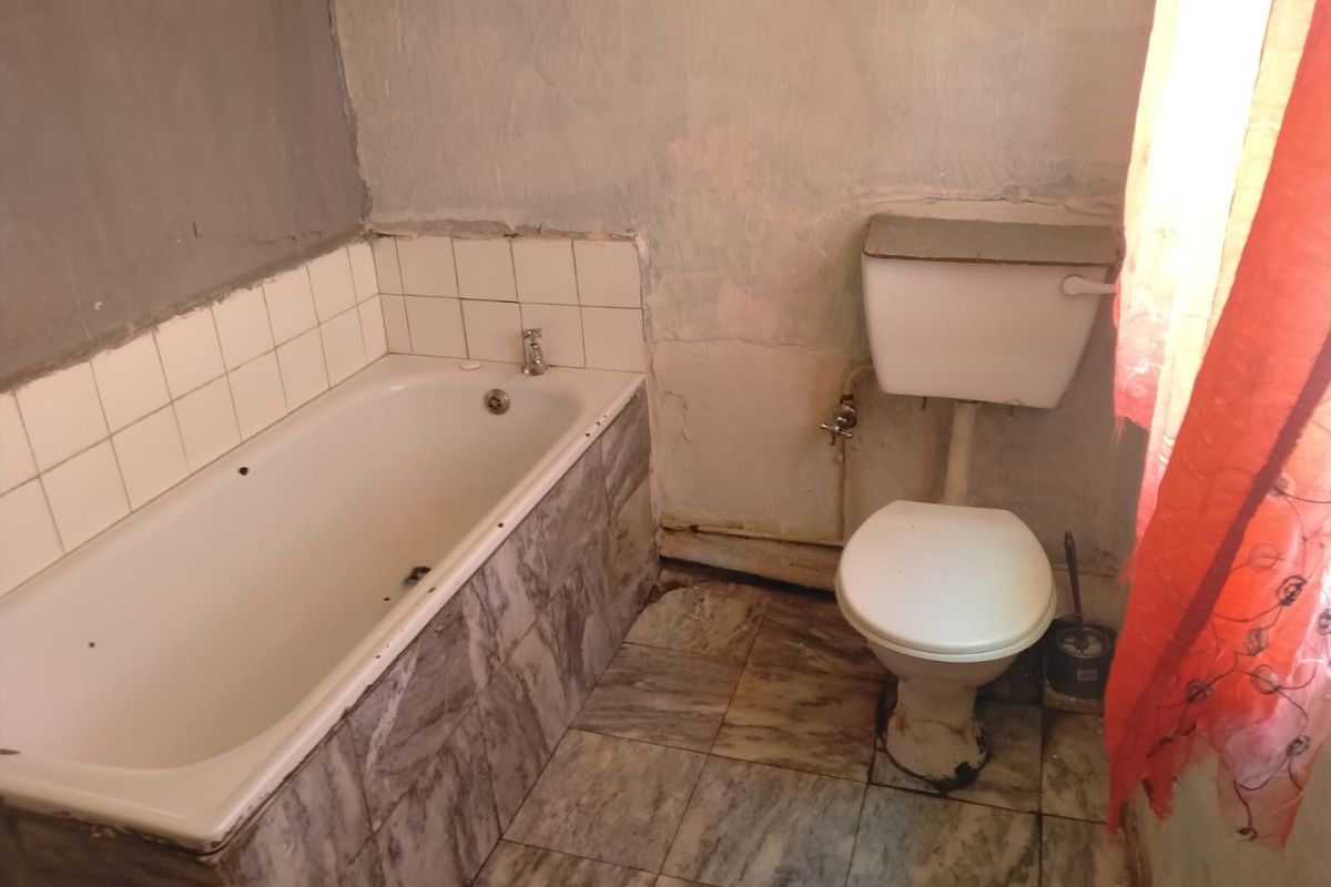 A dated bathroom featuring a built-in bathtub and toilet, requiring significant cosmetic updates and wall repairs to restore its functionality and appeal.