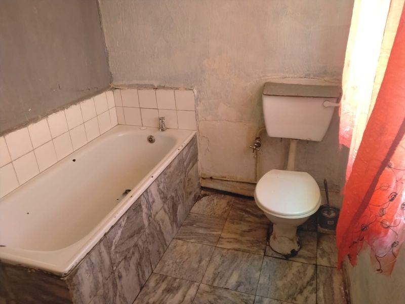 A dated bathroom featuring a built-in bathtub and toilet, requiring significant cosmetic updates and wall repairs to restore its functionality and appeal.