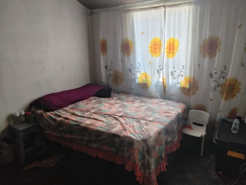 A compact bedroom featuring a window with floral curtains and basic wall finishes, requiring cosmetic updates to improve the overall aesthetic.