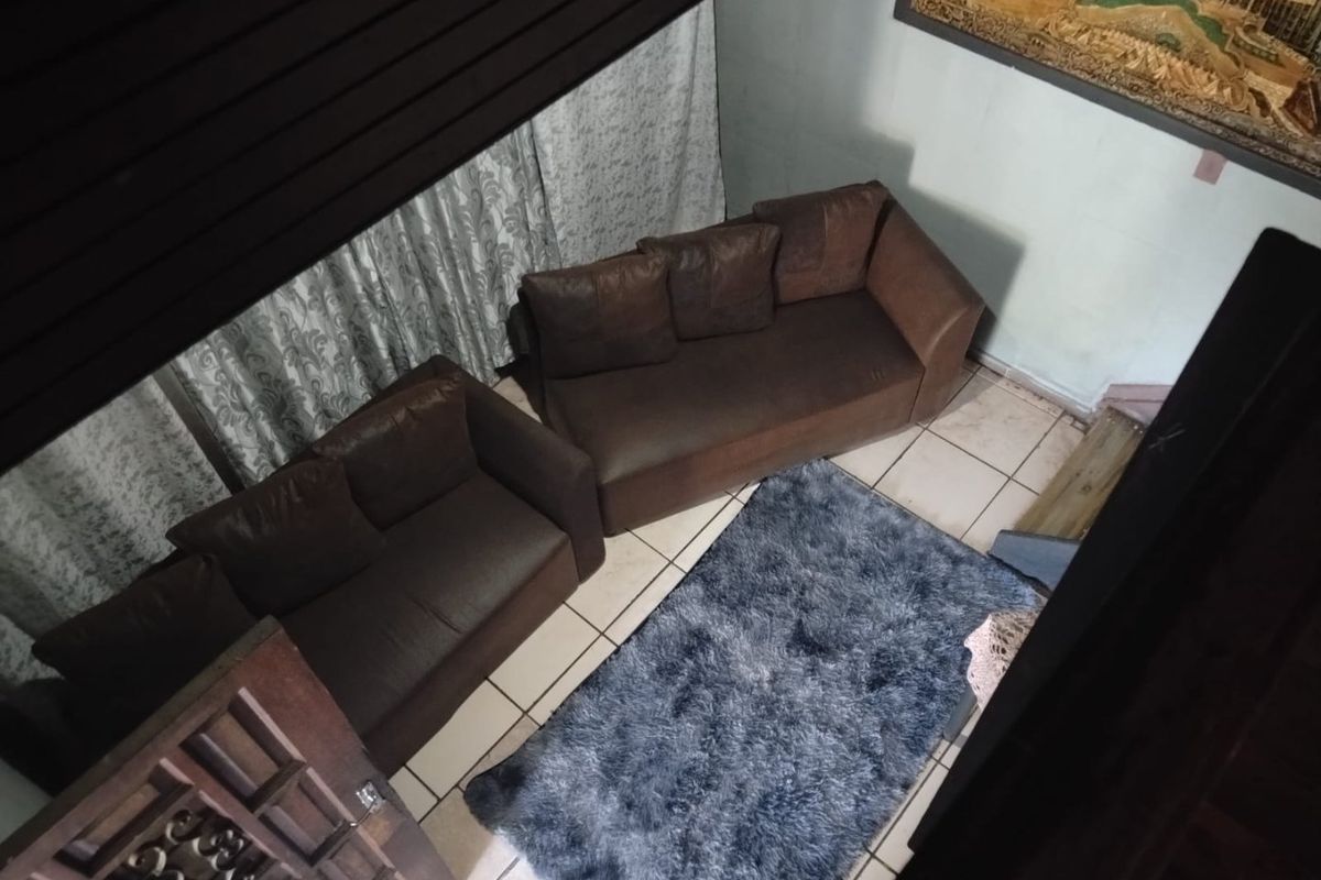 An elevated view of a living room area featuring tiled flooring and a wooden door, showing signs of wear and dated finishes.