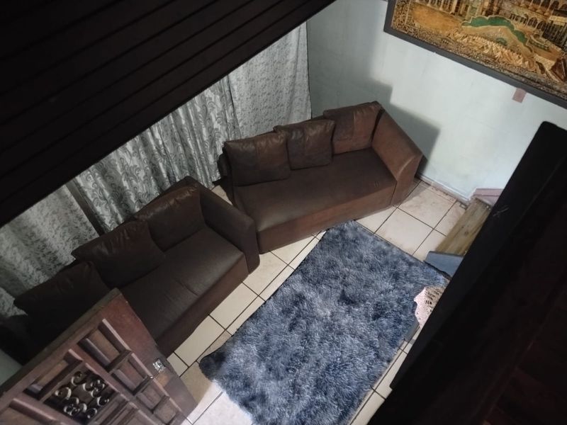 An elevated view of a living room area featuring tiled flooring and a wooden door, showing signs of wear and dated finishes.