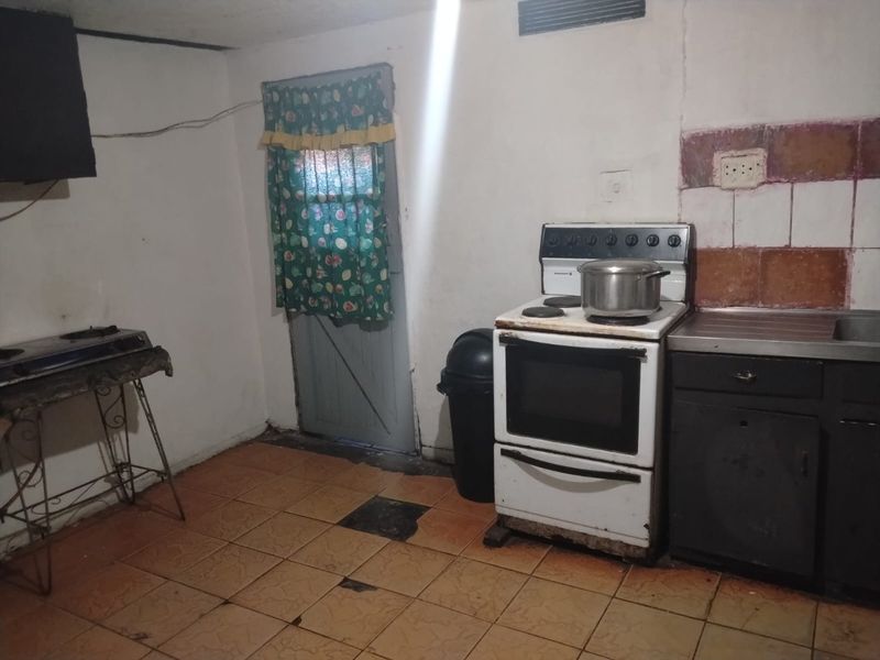 A dated kitchen area featuring tiled flooring, a freestanding stove, and basic cabinetry, requiring significant renovation and cosmetic updates to improve functionality and aesthetic appeal.