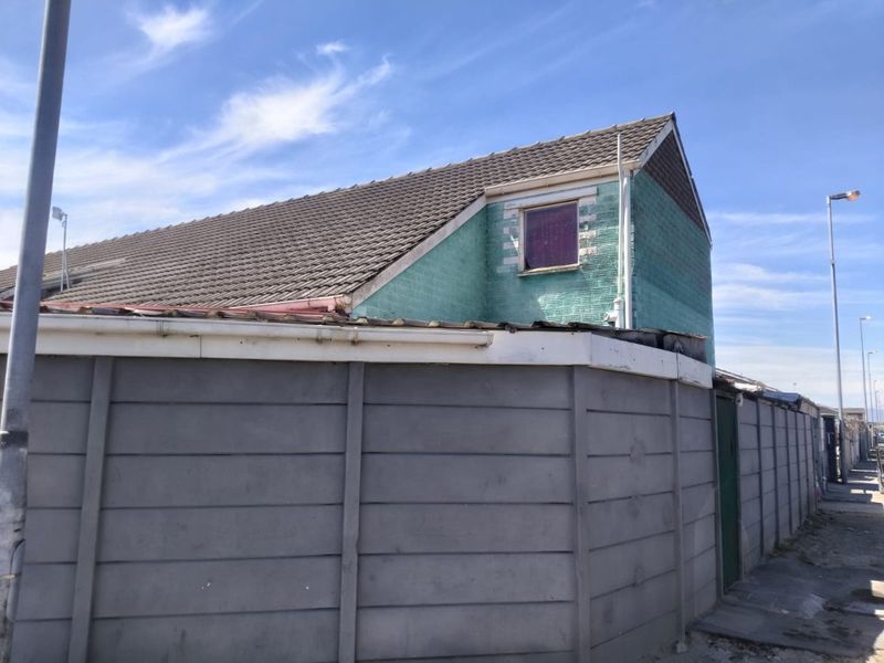 Rear view of the property showing a concrete boundary wall and the exterior facade with visible wear to the paintwork.