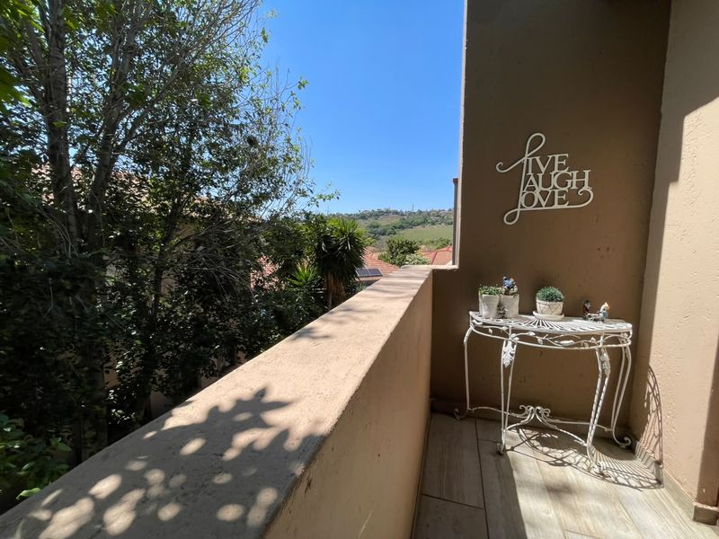 A private balcony featuring tiled flooring and a parapet wall, offering pleasant views of the surrounding trees and landscape.