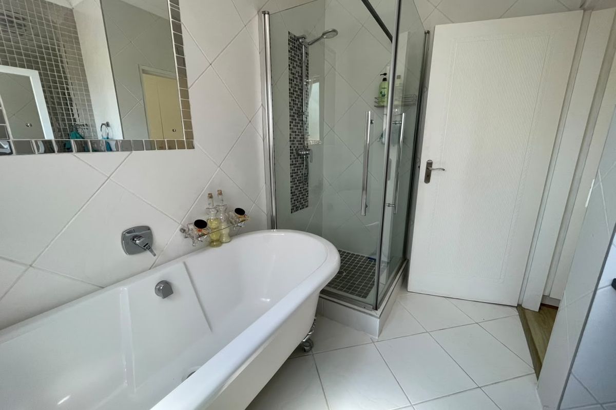 A well-maintained bathroom featuring a classic freestanding bathtub, a separate glass-enclosed shower, and neutral tiled finishes throughout.