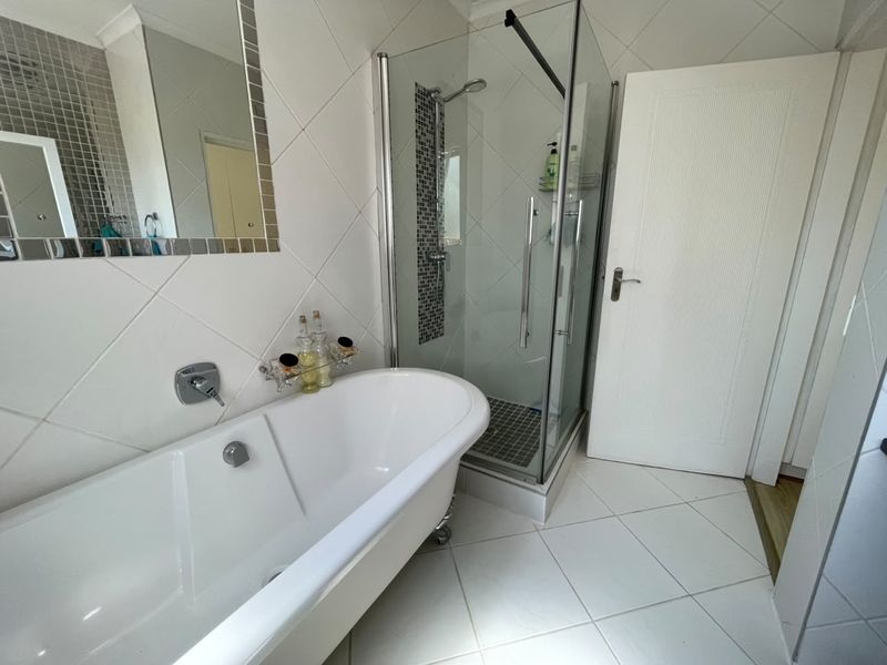 A well-maintained bathroom featuring a classic freestanding bathtub, a separate glass-enclosed shower, and neutral tiled finishes throughout.