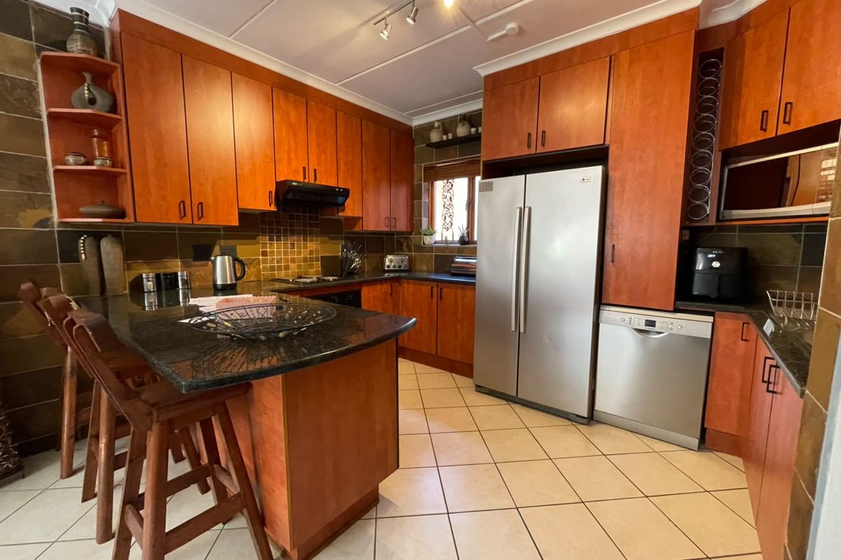 A functional kitchen featuring warm-toned wooden cabinetry, granite countertops, a breakfast bar, and tiled finishes throughout.