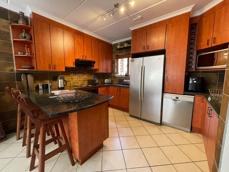 A functional kitchen featuring warm-toned wooden cabinetry, granite countertops, a breakfast bar, and tiled finishes throughout.