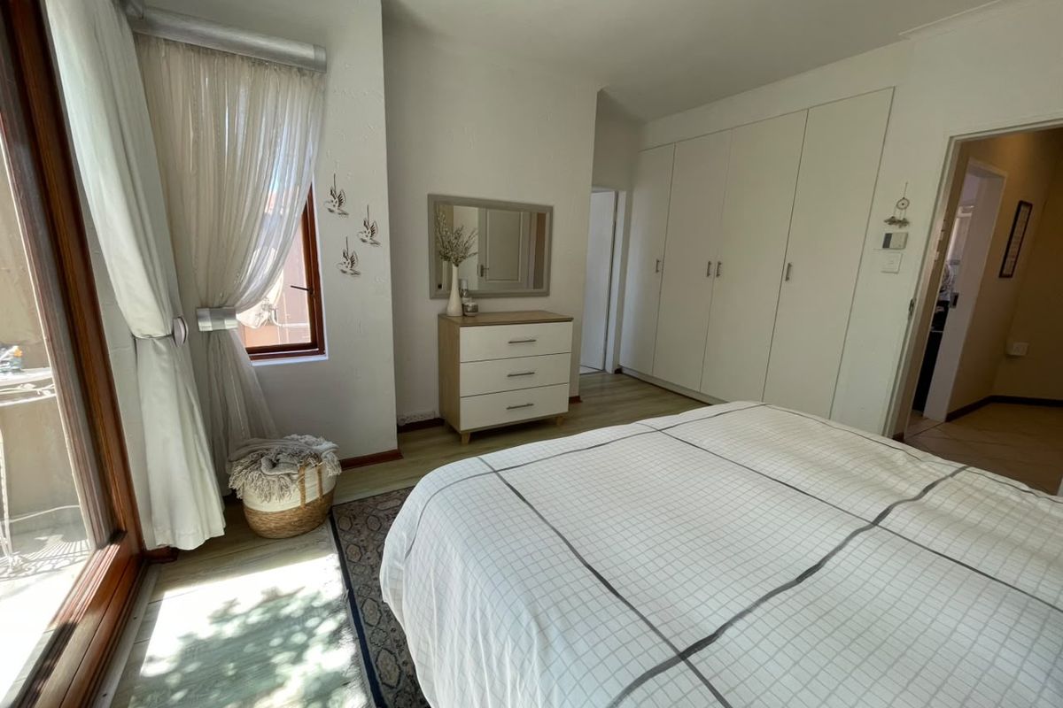 A well-lit bedroom featuring built-in cupboards, laminate flooring, and a sliding door providing access to an outdoor area.