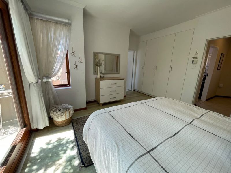A well-lit bedroom featuring built-in cupboards, laminate flooring, and a sliding door providing access to an outdoor area.