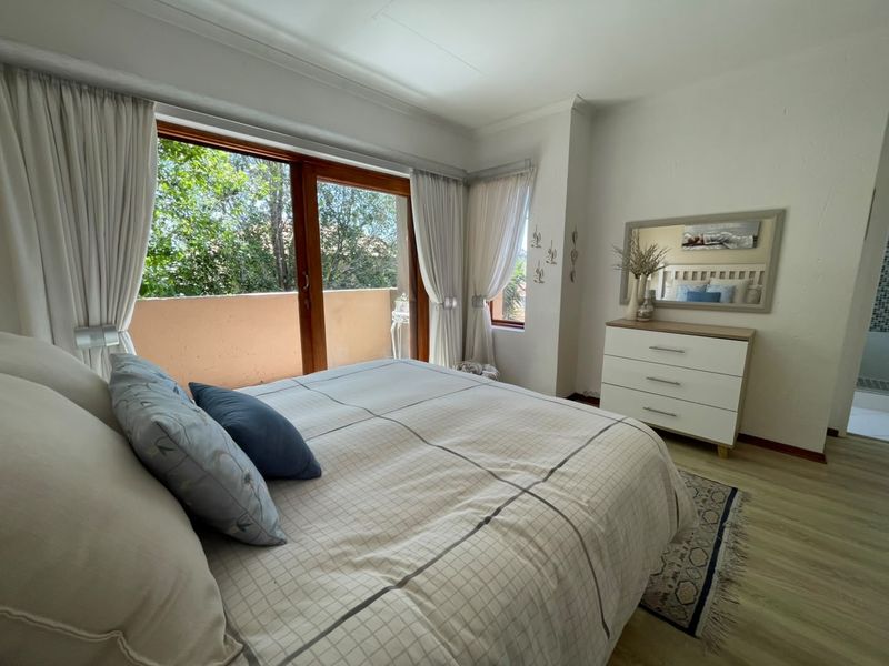 A bright bedroom featuring laminate flooring and a large sliding glass door that opens onto a private balcony with garden views.
