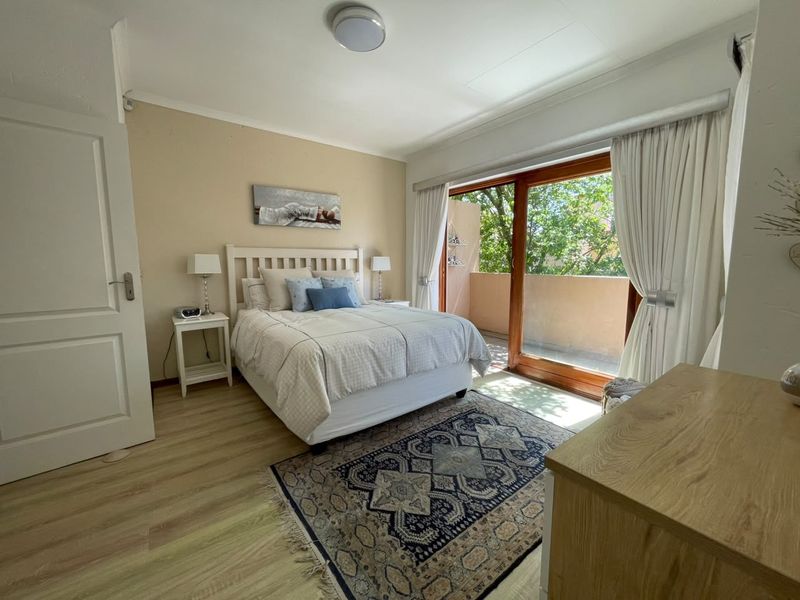 A well-lit bedroom featuring laminate flooring and a large sliding glass door that provides direct access to a private balcony.