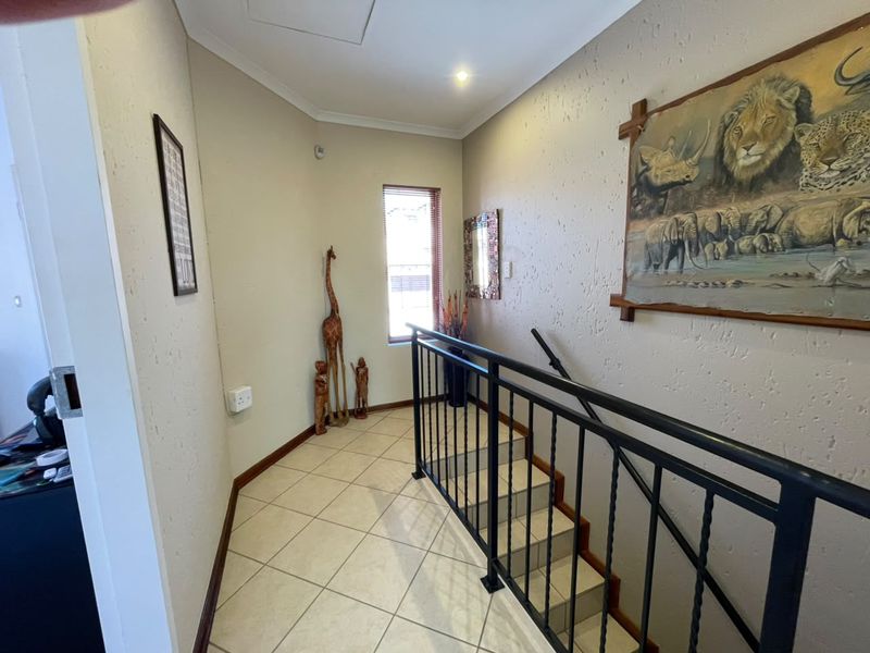 A bright upper-level landing area featuring tiled flooring, a secure wrought iron balustrade, and a staircase leading to the lower level.