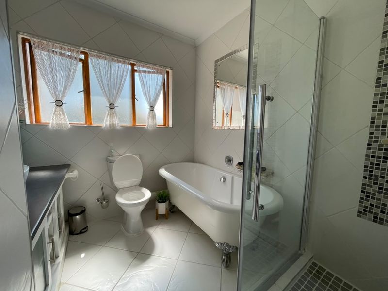 A well-maintained bathroom featuring a classic clawfoot bathtub, a separate glass-enclosed shower, a vanity unit, and neutral wall and floor tiling.