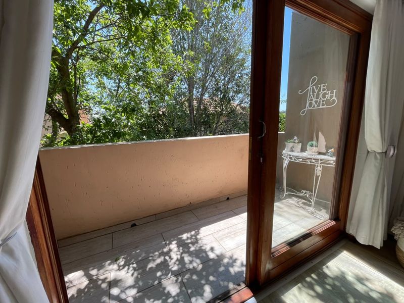 A private balcony featuring tiled flooring and a solid balustrade, accessible through a timber-framed sliding glass door, offering a pleasant outdoor space.