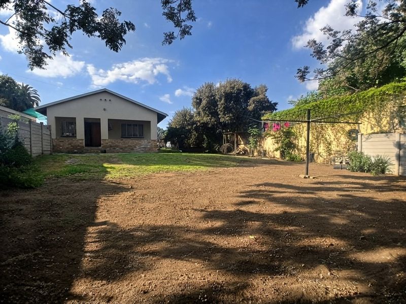A spacious rear garden featuring a covered patio, brick-based house exterior, and a precast concrete boundary wall.