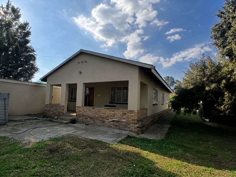 A single-story residential house featuring a covered front porch, brick facade detailing, and a surrounding garden area with a perimeter wall.