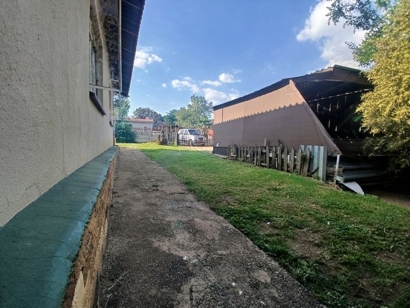 Rear exterior view of the property featuring a concrete pathway, lawn area, and a detached outbuilding structure.