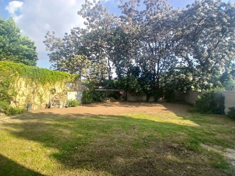 A spacious rear garden featuring a perimeter wall, mature trees, and a central rotary washing line, offering potential for landscaping and outdoor development.