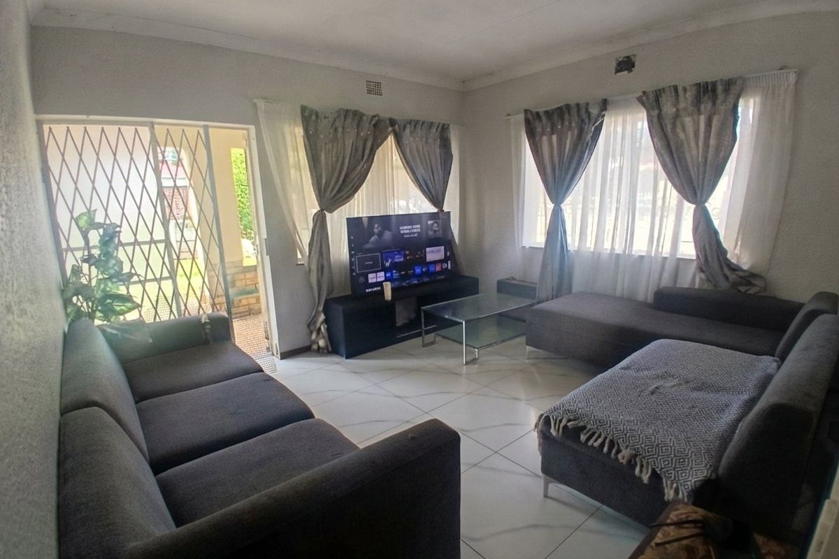 A living room featuring tiled flooring, large windows with curtains, and a security gate leading to the exterior.
