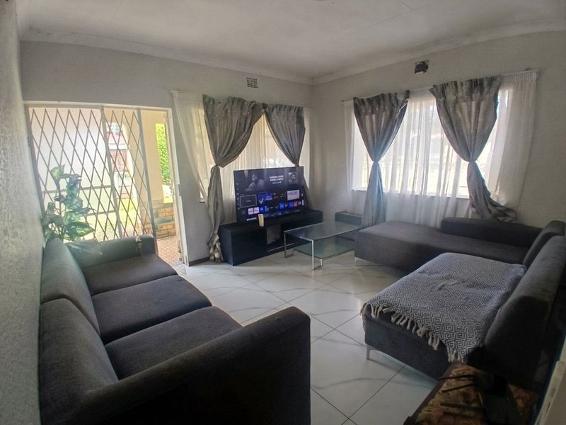 A living room featuring tiled flooring, large windows with curtains, and a security gate leading to the exterior.