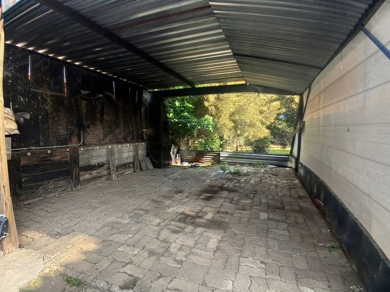 A covered outdoor patio area featuring paved flooring, a corrugated metal roof, and timber retaining walls, offering potential for renovation or outdoor living space.