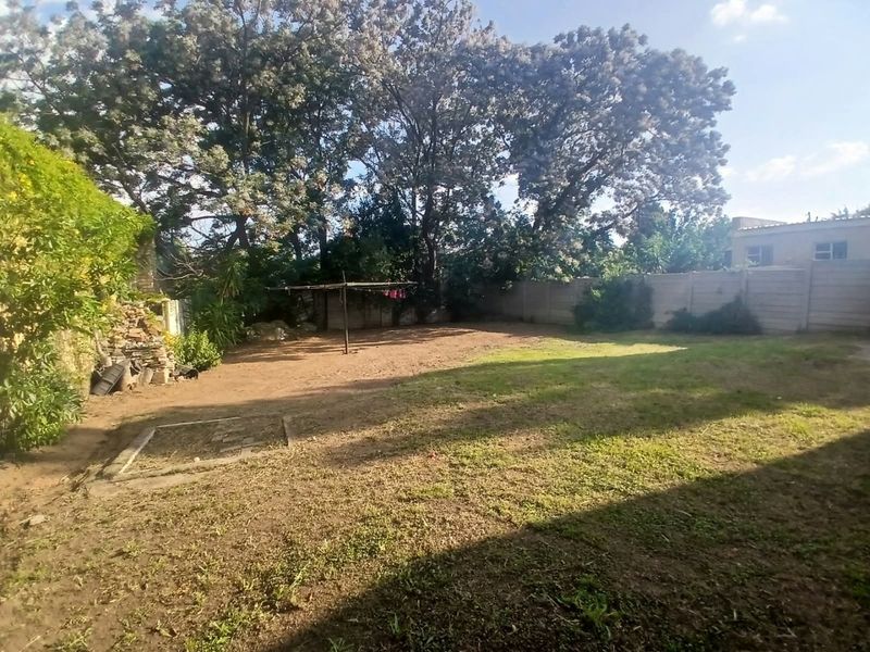 A spacious backyard featuring a large lawn area, mature trees, and a precast concrete boundary wall.
