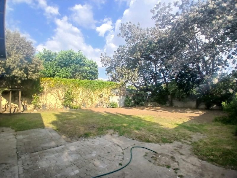 A spacious rear garden featuring a paved patio area, established trees, and a boundary wall, offering potential for landscaping and outdoor living development.