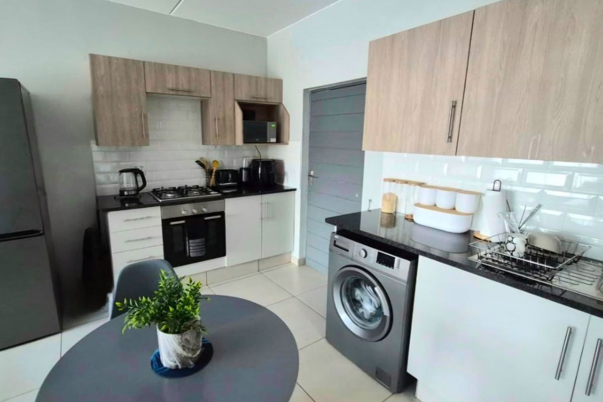 Modern kitchen featuring light wood and white cabinetry, granite countertops, subway tile backsplash, and integrated appliances including a gas hob and washing machine.