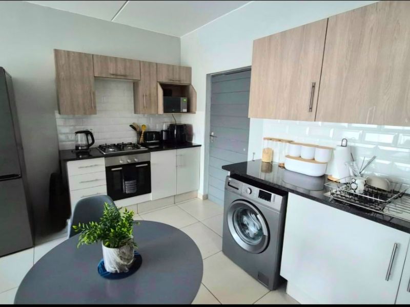 Modern kitchen featuring light wood and white cabinetry, granite countertops, subway tile backsplash, and integrated appliances including a gas hob and washing machine.