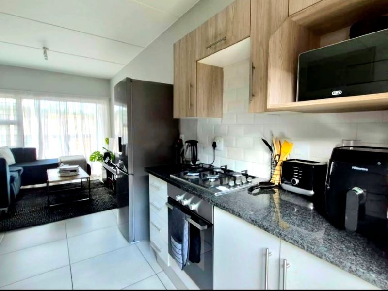 Modern open-plan kitchen featuring granite countertops, subway tile backsplash, and light wood-finish cabinetry, seamlessly flowing into the adjacent living area.