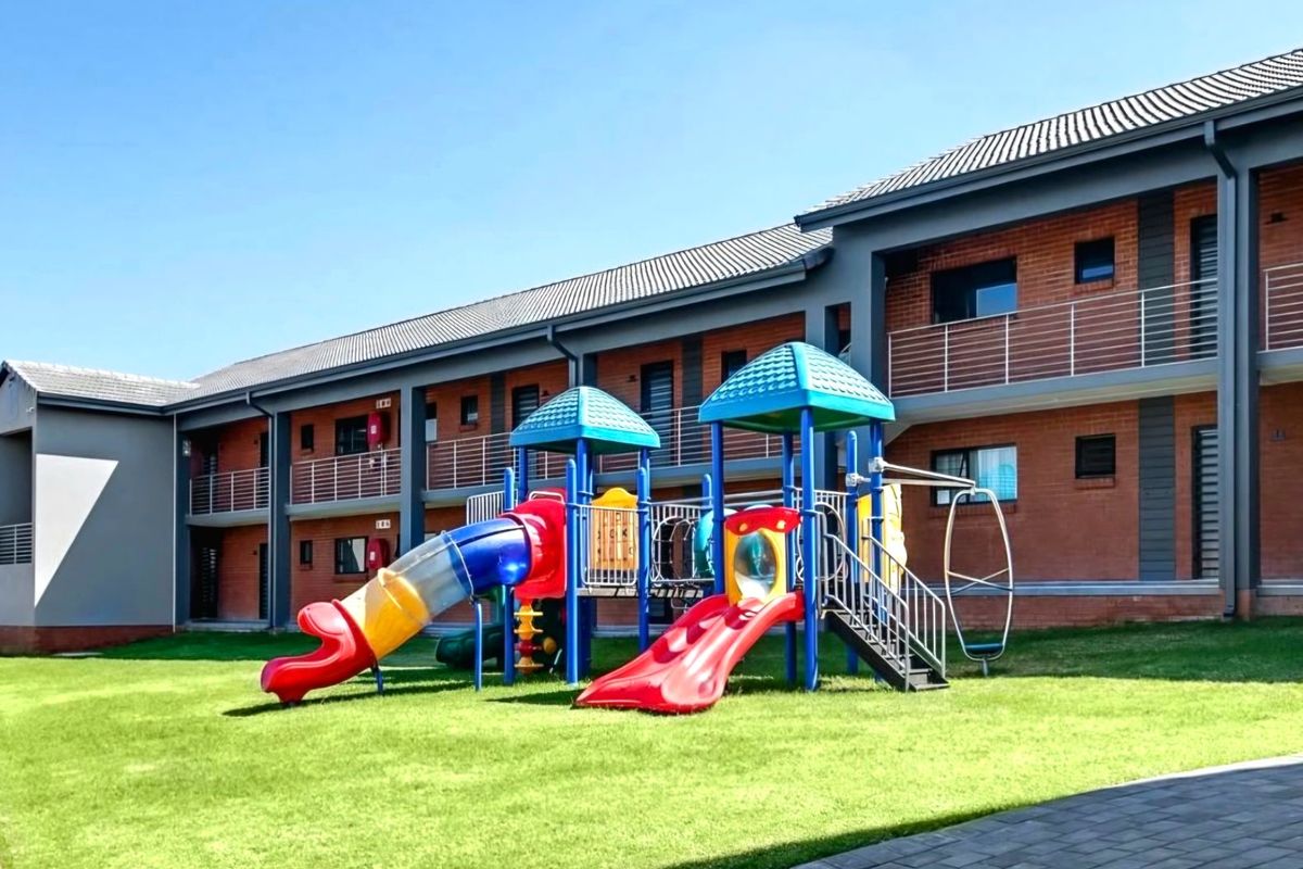Exterior view of an apartment complex featuring a well-maintained communal lawn and a children's playground area.