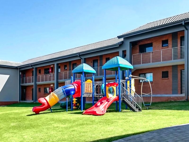 Exterior view of an apartment complex featuring a well-maintained communal lawn and a children's playground area.