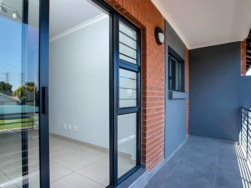 A modern balcony featuring tiled flooring, exposed brickwork, and a sliding glass door providing access to the interior living space.