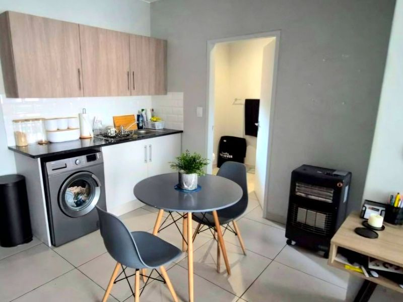Compact open-plan kitchen area featuring modern cabinetry, subway tile backsplash, and tiled flooring, with direct access to an adjacent room.